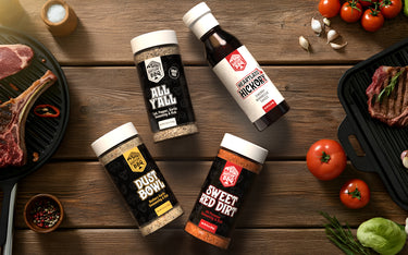 Bartlow's BBQ Sauce and Seasonings on a wooden surface with grilled meat and vegetables